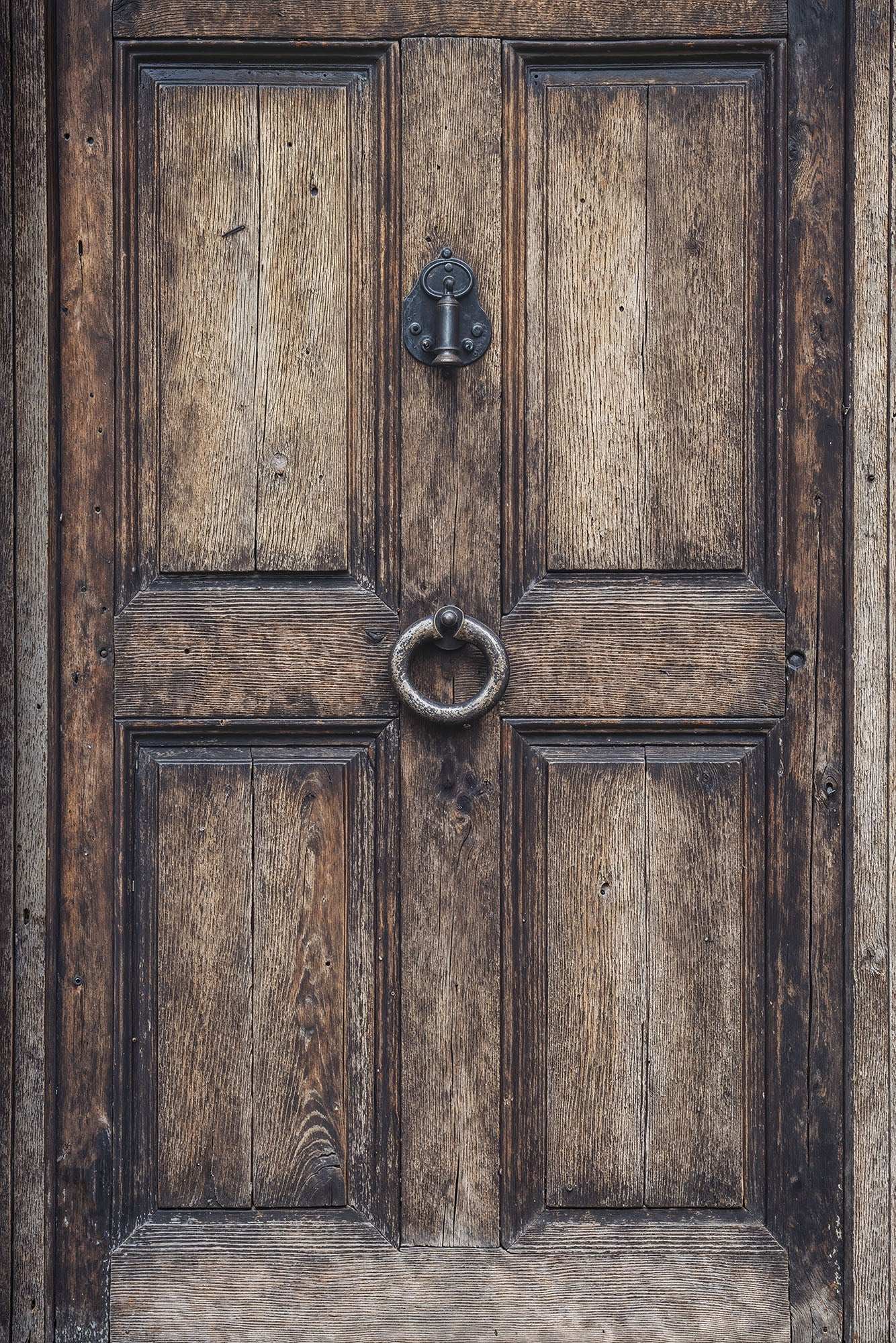 Aged oak door with weathered texture and intricate iron knocker, perfect for rustic and vintage photography settings.