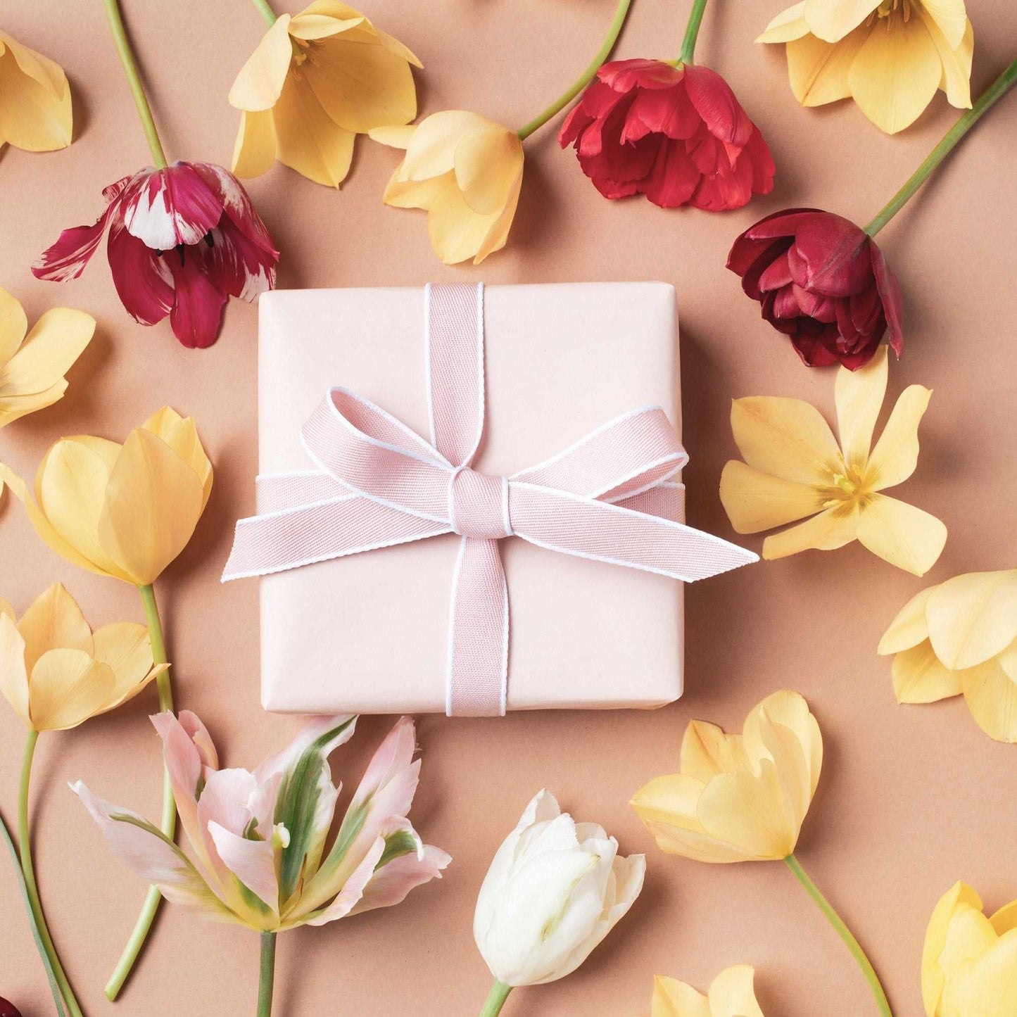 Warm Almond background with colorful flowers and a gift box, perfect for elegant photography settings.